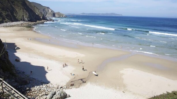 Una spiaggia con persone che camminano e siedono, una scogliera rocciosa e l'oceano.