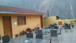 An outdoor patio area with tables and chairs, potted plants, and a building with a red roof and orange walls. - Hotel with two terraces overlooking the mountains and the temple of the Inca sun (OLLANTAYTAMBO)