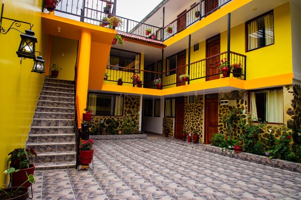 A multi-level building with a yellow exterior, multiple balconies with potted plants, and a tiled courtyard.