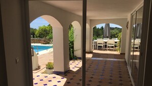 A view through a glass door into a patio area with a pool, outdoor furniture, and a tiled floor. - Lovely Andalucian villa in a quiet, green neighborhood (Estepona)