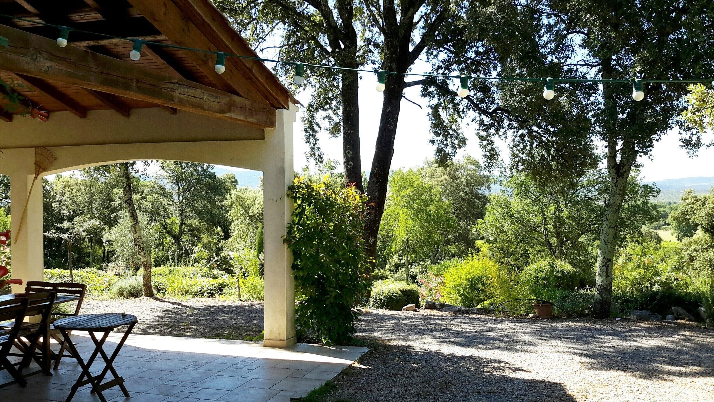 Een buitenpatio met een pergola, zitplaatsen en lichtjes.