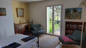 A room with a bed, a chair, a desk with a lamp, a bookshelf, and a large window with a view of greenery. - house - 4 rooms - 4/6 persons (Conqueyrac)