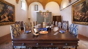 A long dining table with chairs, a chandelier, wine bottles, and a pizza.