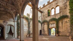 An interior courtyard with arches, columns, and a stone wall with vegetation.