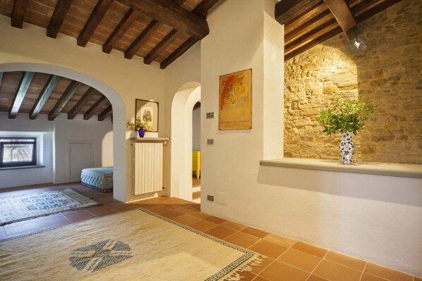 Una habitación con vigas de madera a la vista, pared de piedra, ventana con planta y alfombra estampada.