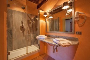 A bathroom with a glass-enclosed shower, a vanity with a mirror, and a hairdryer mounted on the wall.