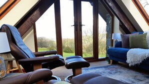 Una habitación acogedora con un ventanal grande, un sofá azul y dos sillones reclinables.
