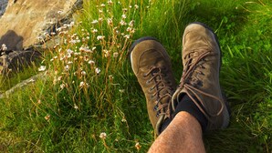 Un par de botas de senderismo sobre una zona cubierta de hierba, con una orilla rocosa y el océano al fondo.