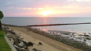 Una playa con costa rocosa, un paseo de madera y un atardecer sobre el agua.