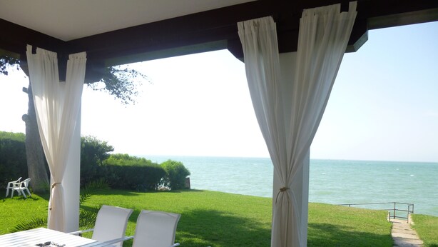 Un porche techado con una mesa y sillas, con vistas a un área verde y al mar.