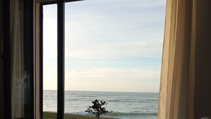 Un dormitorio con un ventanal grande con vistas al mar, una cama con colcha estampada y una bandeja con tetera y taza.