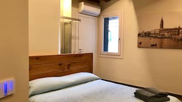 A bedroom with a wooden headboard, a bed with white bedding, a window with a view of a cityscape, and a wall-mounted air conditioning unit.