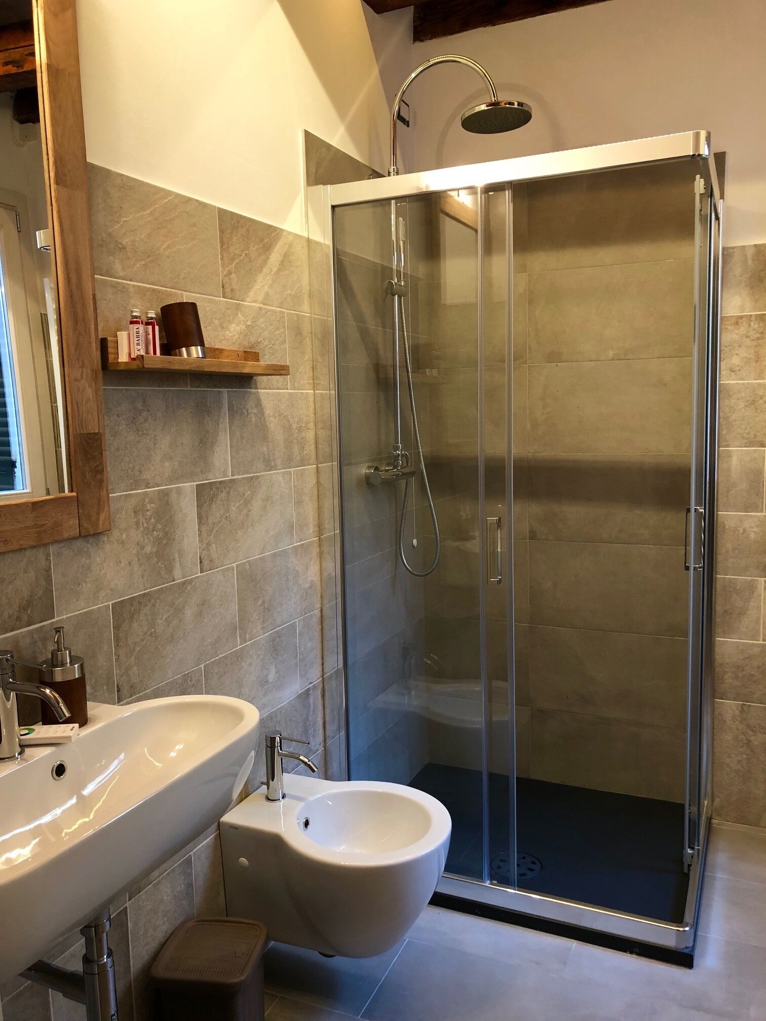 A modern bathroom with a glass-enclosed shower, a pedestal sink, and a bidet.