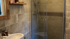 Un baño moderno con ducha envuelta en vidrio, lavamanos pedestal y bidé.