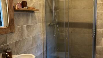 A modern bathroom with a glass-enclosed shower, a pedestal sink, and a bidet.