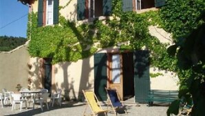 A building with a rustic facade, partially covered in ivy, featuring a small patio with outdoor seating and a table. - Character house surrounded by vineyards 6 pers (Bollène)