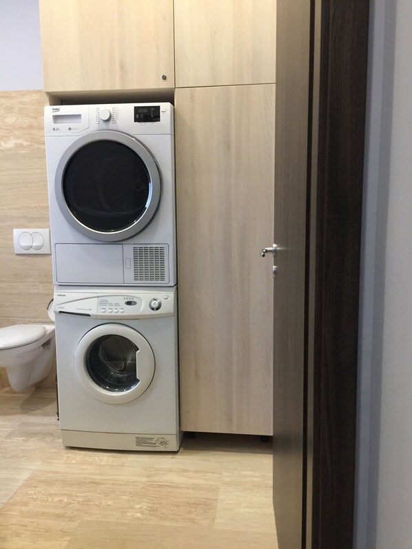 Un appareil compact combinant lave-linge et sèche-linge, installé dans une petite buanderie avec un meuble en bois et des toilettes.