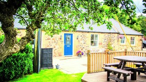 A stone building with a blue door, a wooden deck, and picnic tables.