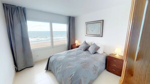Un dormitorio con un ventanal grande, una cama con ropa de cama estampada, dos mesitas de noche con lámparas y un cuadro en la pared.