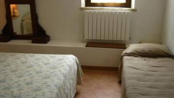 Une chambre avec deux lits simples, un radiateur, une fenêtre et un miroir au mur.