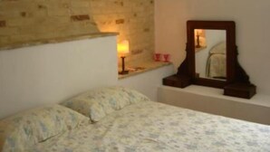 Ein Schlafzimmer mit Backsteinwand, einem Bett mit floralem Bettbezug, einem Nachttisch mit Lampe und einem Spiegel.