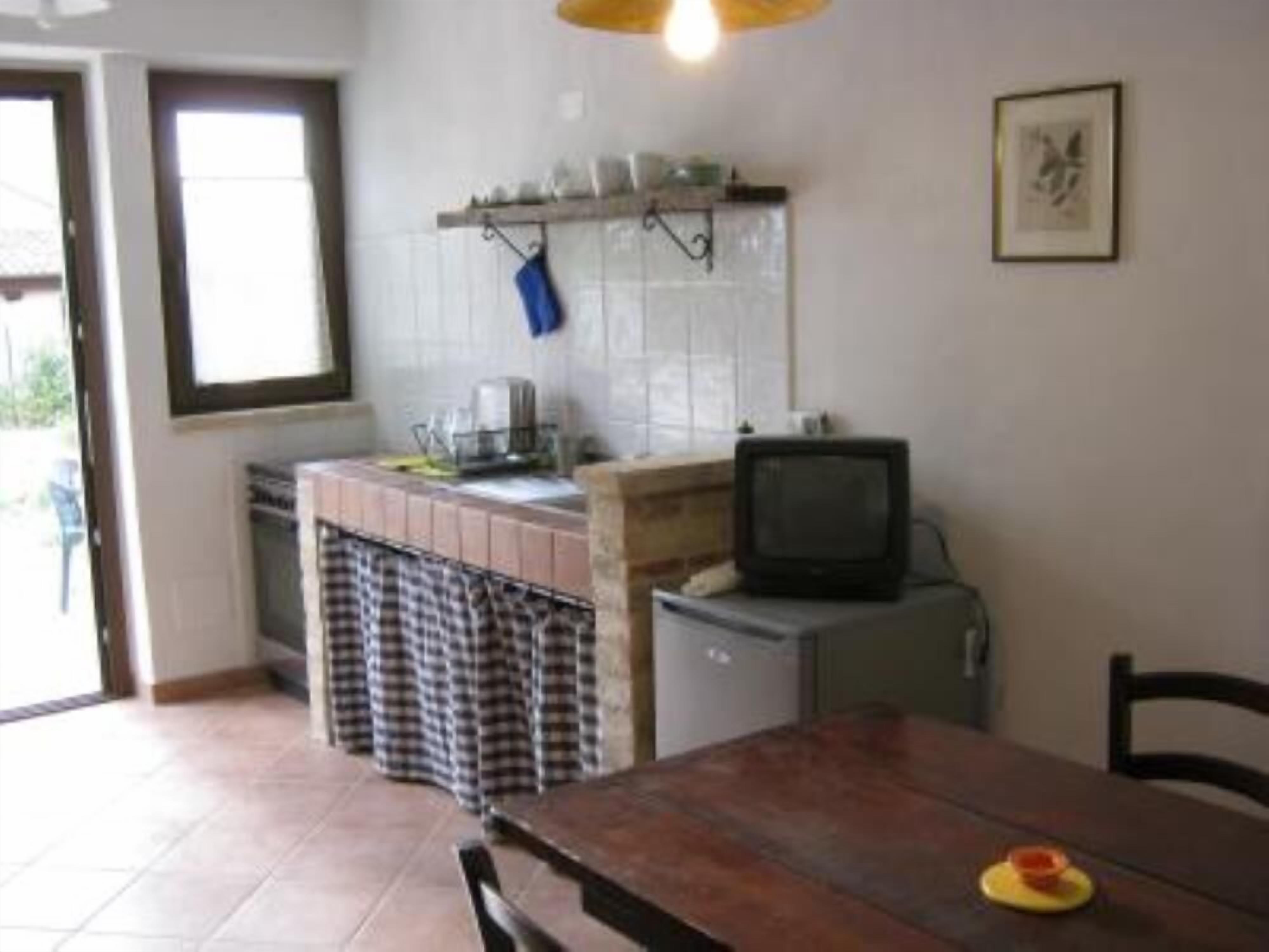 Ett kök med kakel på väggen bakom arbetsbänken, ett litet kylskåp, en tv och ett matbord med stolar.