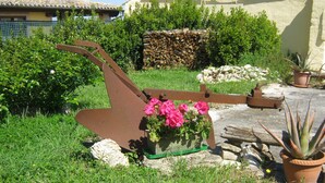 Ein Garten mit einer verrosteten Metallkonstruktion, Blumentöpfen und einer Steinmauer.