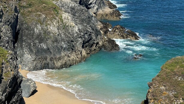 A coastal landscape with a sandy beach, rocky cliffs, and the ocean.