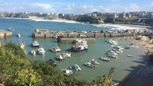 A coastal harbor with boats docked, a sandy beach, and a town in the background.