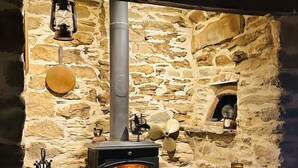A stone-walled room with a wood-burning stove, a lantern, and a basket of firewood.