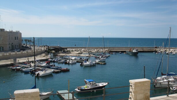 Un puerto deportivo con varias embarcaciones amarradas, un muelle que se adentra en el agua y un edificio a la izquierda.