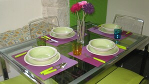 Una mesa de comedor dispuesta con platos verdes, un jarrón de vidrio transparente con flores y un vaso de líquido ámbar.