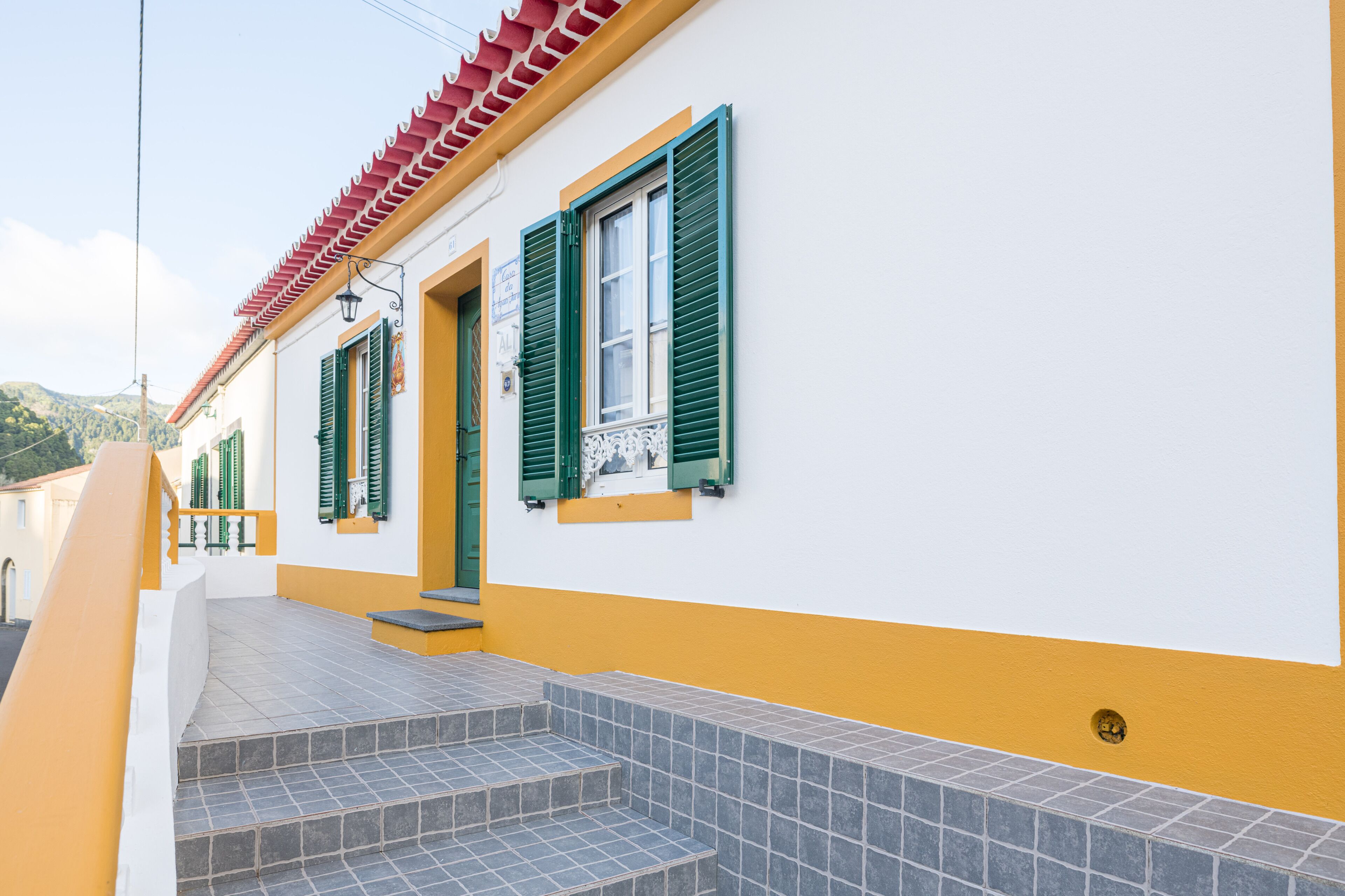 A building with a yellow and white facade, green shutters, and a tiled staircase leading to the entrance.