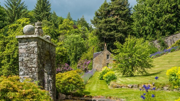 A stone structure with a small building in a lush garden setting.