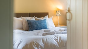 A neatly made bed with white linens and blue and beige pillows, a lamp with a patterned shade, and a key in the foreground.