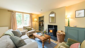A cozy living room with a sofa, a wooden coffee table, a fireplace, and a window with curtains.