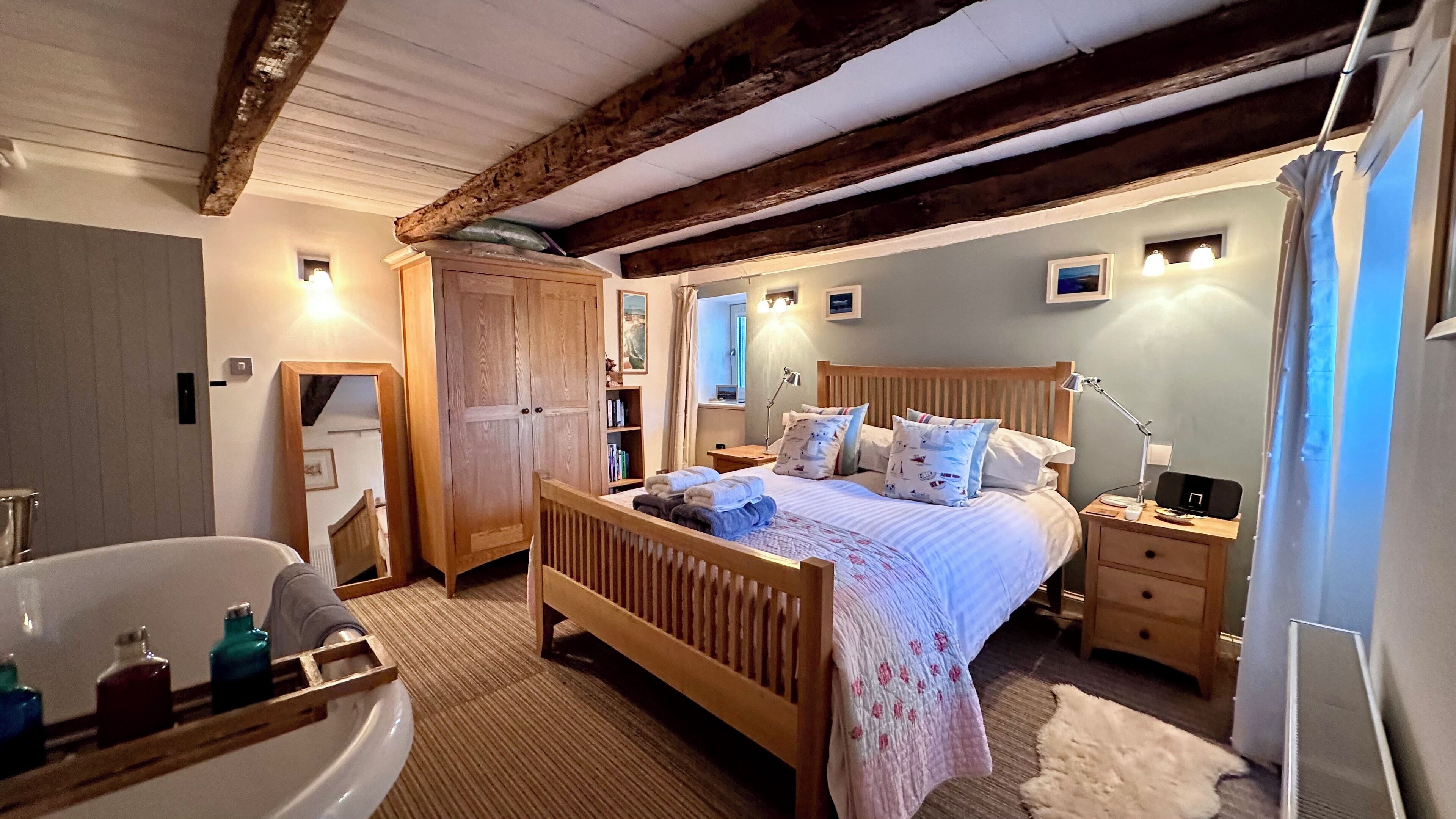 Un dormitorio con cama de madera, mesitas de noche, tocador, espejo, armario y baño con bañera y artículos de aseo.