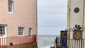 A coastal building with a pink facade, a red railing, and a stone staircase leading to a gate.