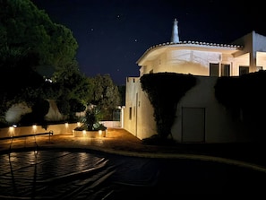 Vista nocturna d'un edifici amb cúpula i torre, envoltat d'arbres i una zona pavimentada amb llums.