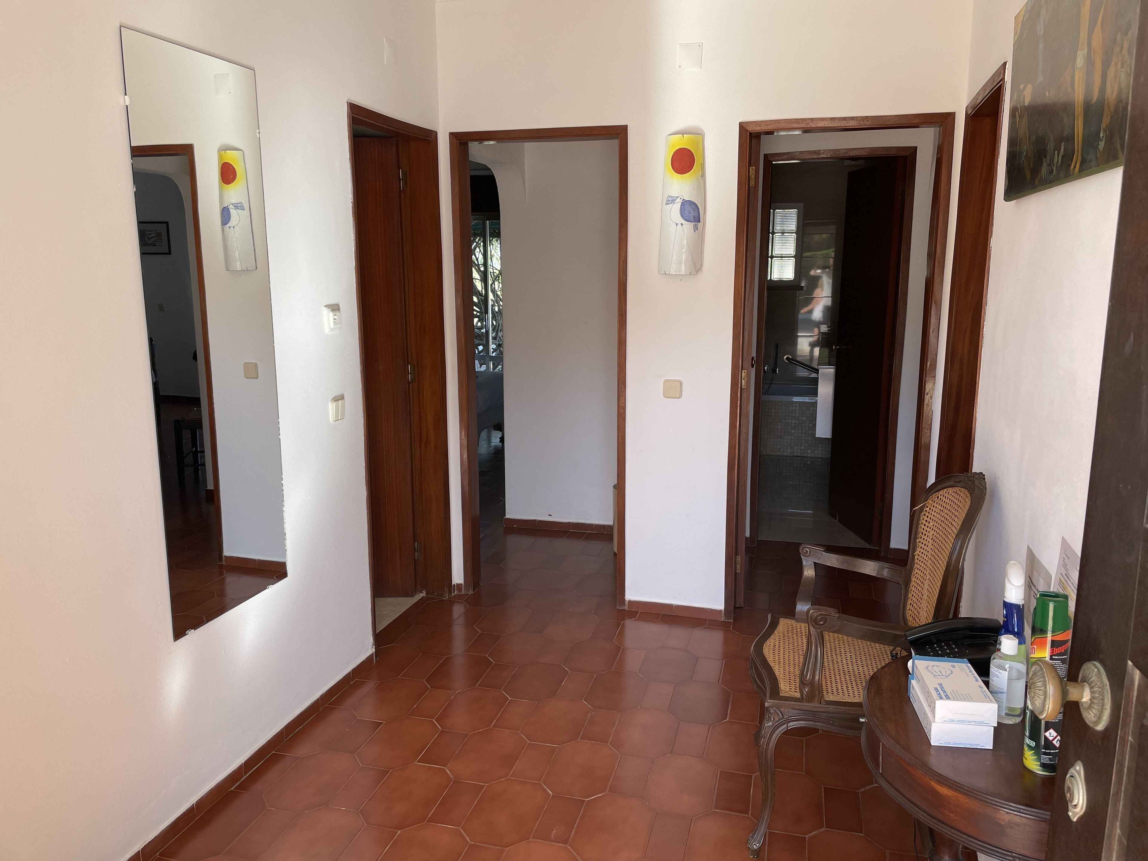 A hallway with tiled flooring, wooden doors, and a chair with items on a small table.