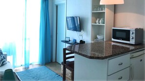 A compact kitchen with a microwave, a small shelf with dishes, and a TV mounted on the wall. - Bright Seafront Apartment In Funchal with Sea View from the Balcony (Funchal)
