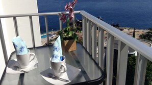 A balcony with a glass table, two white cups with floral designs, a spoon, and a potted orchid. - Bright Seafront Apartment In Funchal with Sea View from the Balcony (Funchal)
