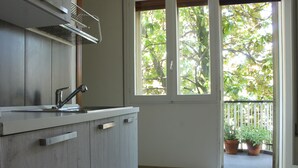 A kitchen with a modern design, a window with a view of trees, and a balcony with potted plants.