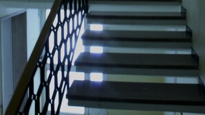 A staircase with a black metal railing and a vase on the landing.
