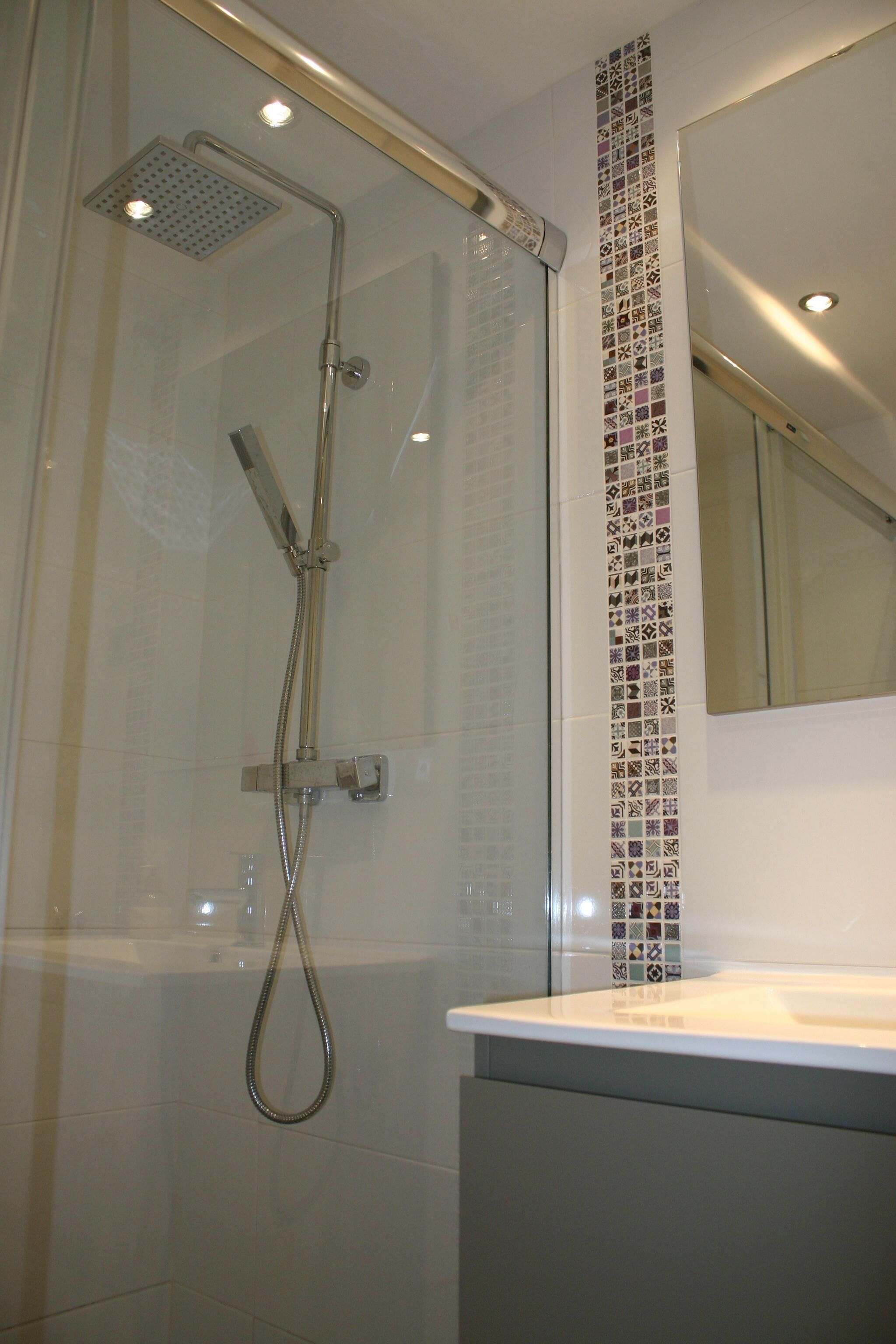 A shower with a glass door, a handheld showerhead, and a wall-mounted control panel.