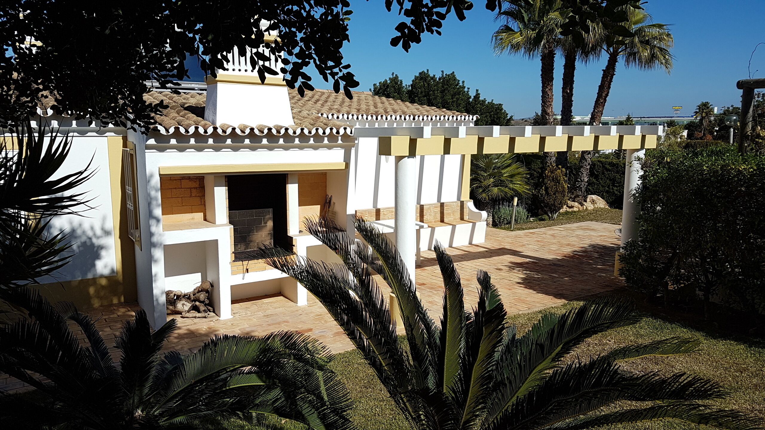 A small, white building with a tiled roof, surrounded by palm trees and a paved area.
