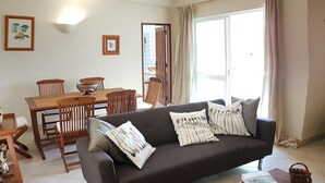 Ein Wohnzimmer mit einem dunkelbraunen Sofa, einem Holzesstisch mit Stühlen, einer schwarzen Ledercouch und einem Couchtisch aus Holz.