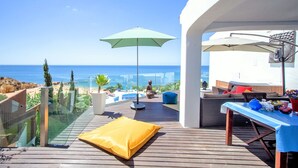Una terraza de madera con piscina, mobiliario exterior y vista al mar.