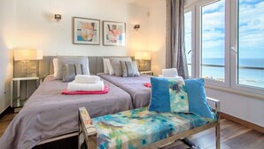 Habitación de hotel con dos camas, vista al mar y obras de arte en la pared.