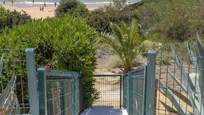 Un camino que lleva a una playa con vistas despejadas al océano y gente en la arena.